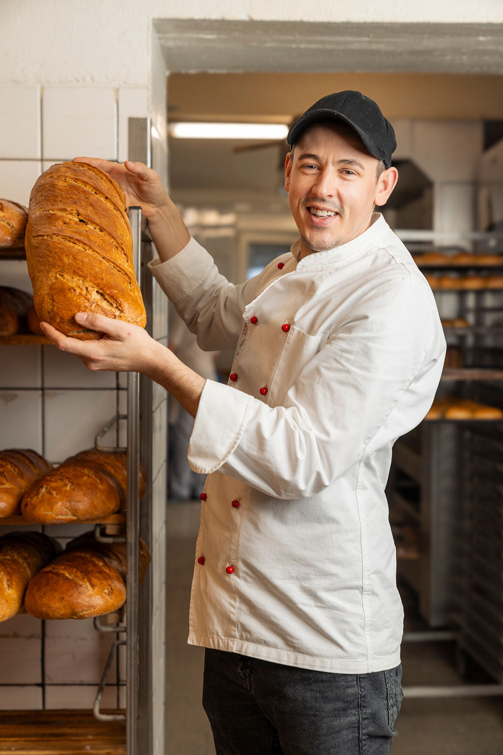 Bäcker der Bäckerei Lehmann mit einem frisch gebackenen Brotlaib vor den Brotregalen